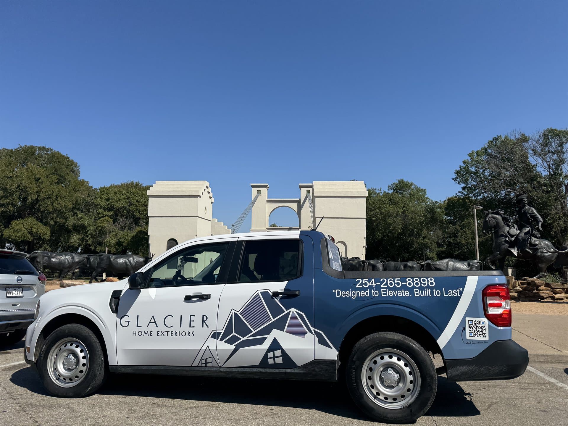 Glacier Home Exteriors truck at the historic Waco Suspension Bridge with cattle drive sculptures